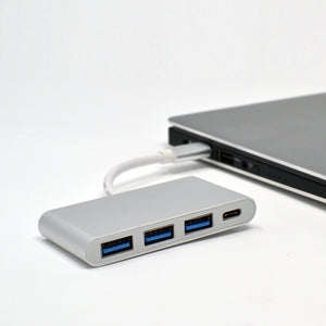 A silver 4 in 1 USB C hub with three USB 3.0 ports and one USB Type C port, connected to a laptop.