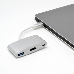 A silver USB Type C hub connected to a laptop, with HDMI and USB cables alongside.