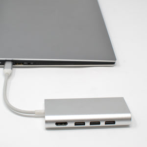 A silver USB C hub with multiple ports including HDMI, Ethernet, SD/TF card reader, and USB Type-C, connected to a laptop.